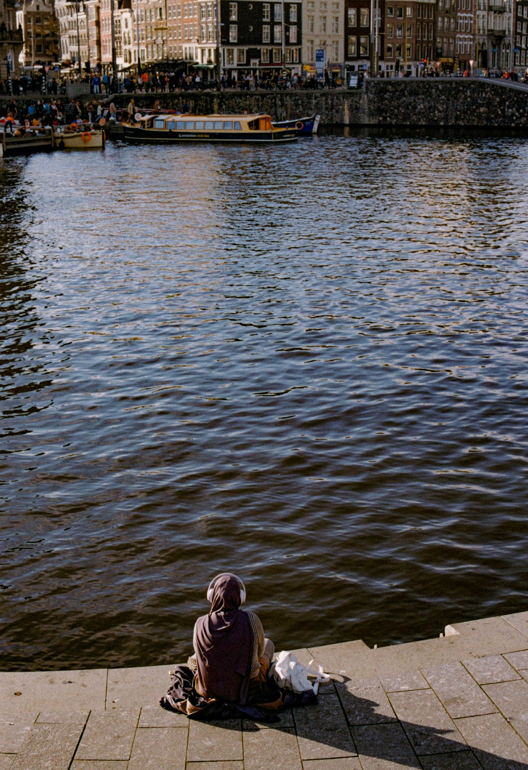 Person sits by the water in an urban setting.
